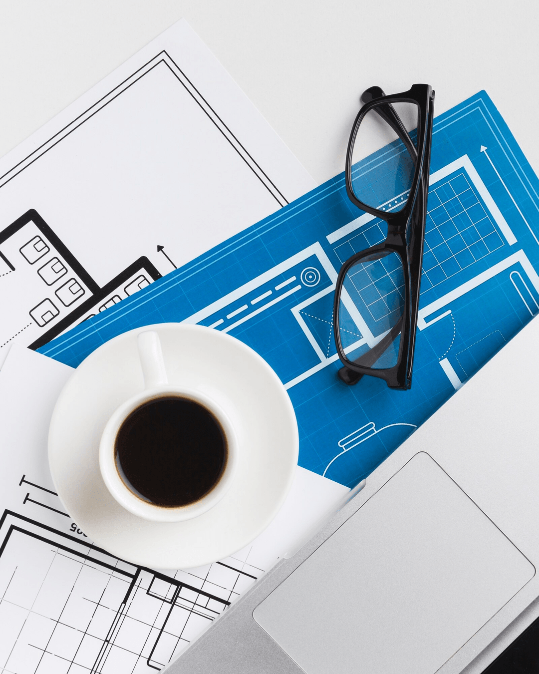 Project workspace with blueprints, coffee cup, and glasses